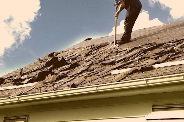 damaged roof with worker removing shingles