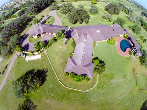 Aerial view of large estate building with pool and brown luxury roof