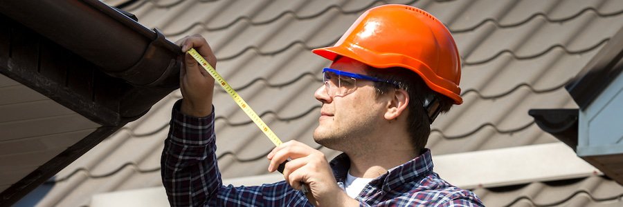 A roof inspector performing a roof inspection using a tape measurer.